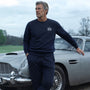 Man in James Bond Sweatshirt standing next to a classic Aston Martin DB5 Silver Birch with a cloudy sky background