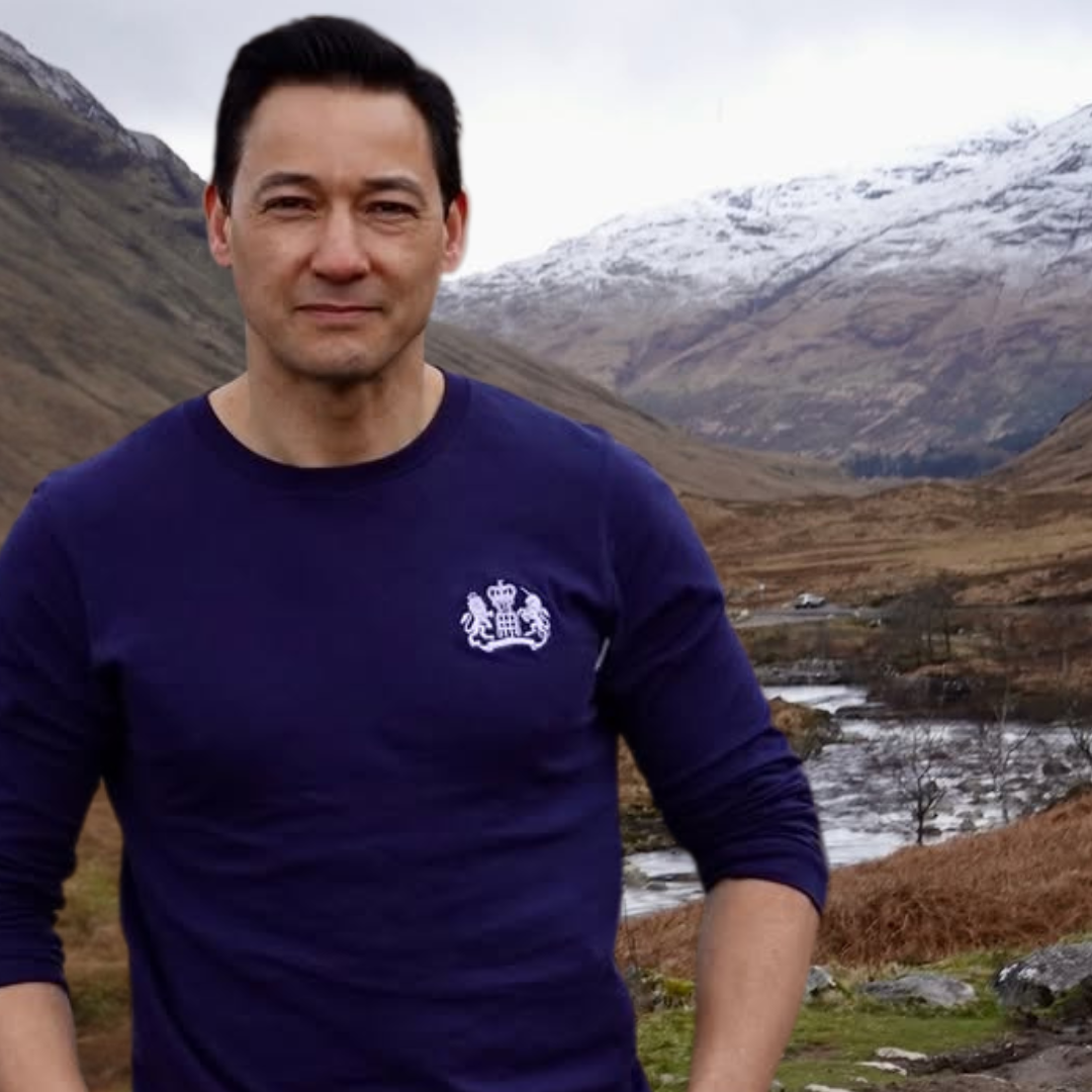 Man wearing a navy blue James Bond long sleeve shirt as seen in Skyfall with a S.I.S. logo in front of the famous Skyfall filming location photo spot.