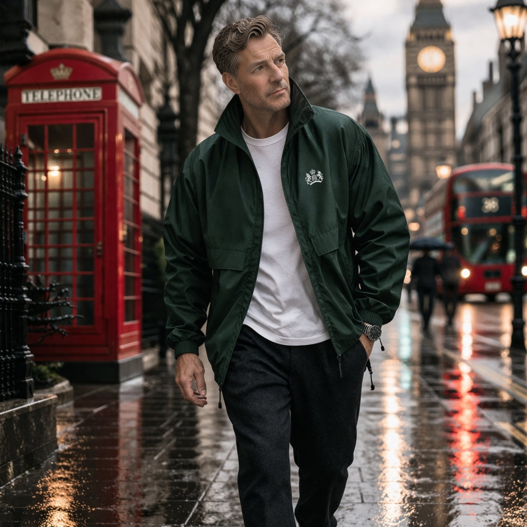 Man walking on a rain-soaked street with a red telephone box and double-decker bus in the background wearing a Green James Bond Windbreaker