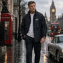 Man standing in a rain-soaked street with iconic London landmarks in the background wearing James Bond Navy coloured Windbreaker