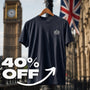 A James Bond inspired navy blue short-sleeve t-shirt with a small white S.I.S. Logo embroidered on the left chest, hanging on a wooden hanger against a blurred background of Big Ben and a Union Jack flag. A large white '40% OFF' graphic overlay is in the foreground.