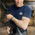 Man holding a rifle in an urban setting with a blurred background wearing a James Bond T-Shirt