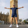 Person in athletic t-shirt standing with arms outstretched in front of Big Ben, London.