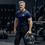 Man holding a weight plate in a gym setting wearing a James Bond T-Shirt with Embroidered S.I.S. Logo from Skyfall