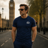 Man wearing a navy blue James Bond Skyfall t-shirt with a logo in front of Big Ben in London England