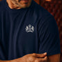 Man wearing a James Bond Navy blue t-shirt with a white emblem worn by a person, against a blurred background.