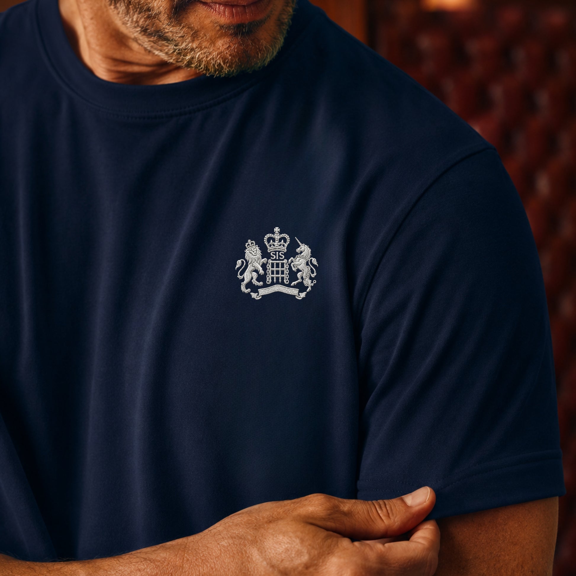 Man wearing a James Bond Navy blue t-shirt with a white emblem worn by a person, against a blurred background.