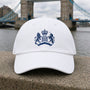 White James Bond Hat with Embroidered S.I.S. Logo from Skyfall on a stone ledge with a bridge and river in the background